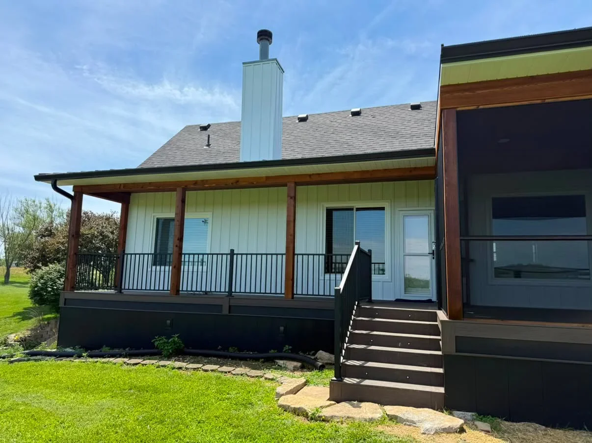 White painted farmhouse exterior with wood beam porch, metal railings, and gray roof
