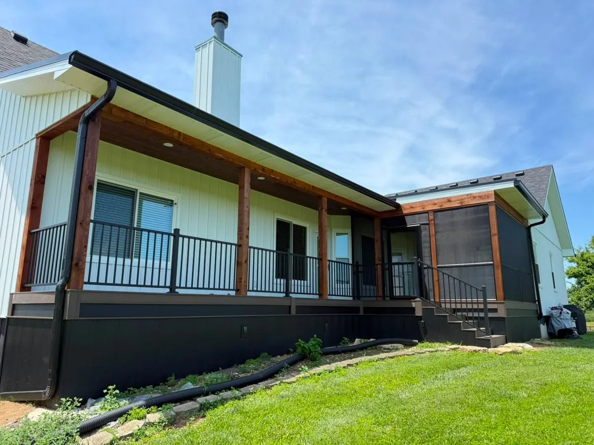 White metal siding farmhouse with sage green soffit, wood beam porch, and black metal railings