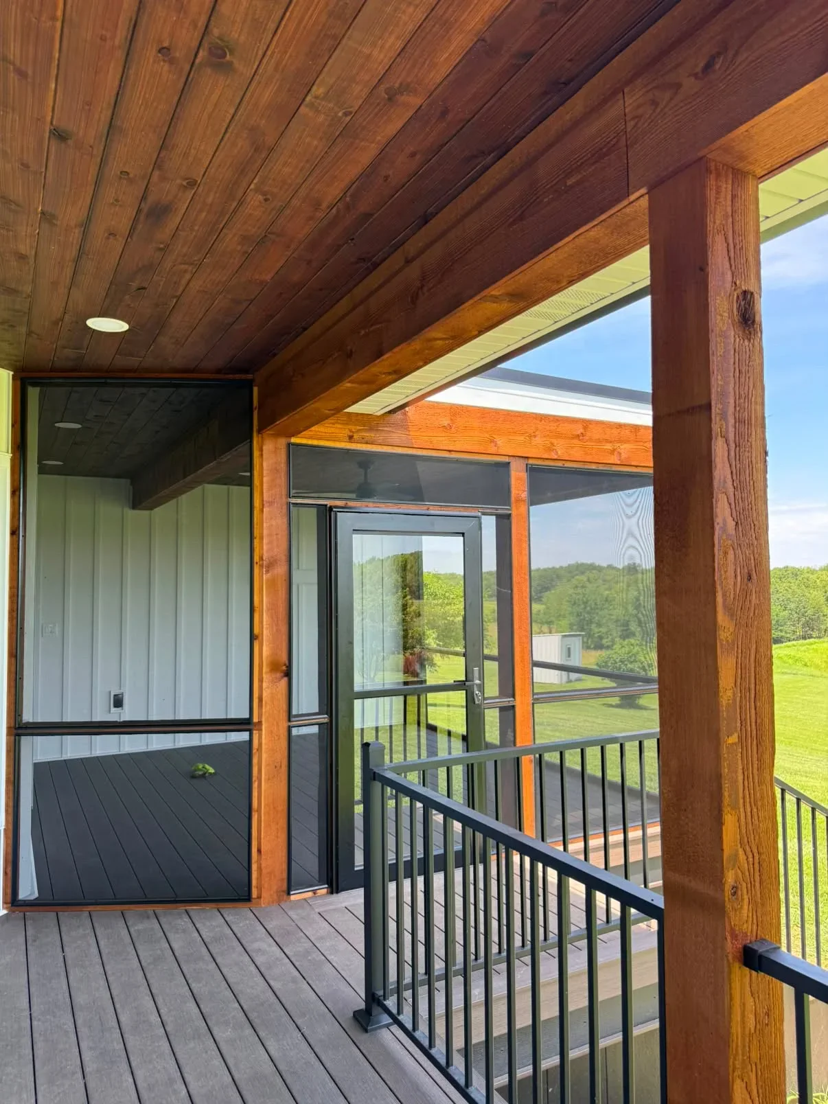 Covered deck with stained wood ceiling beams, painted trim, black metal railings, and screened door