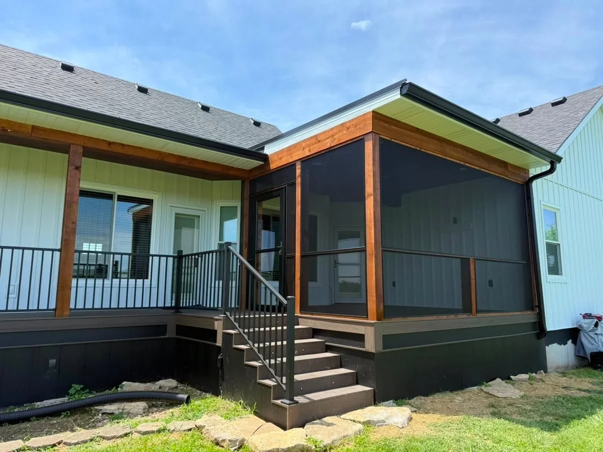 Green vertical siding house with black-screened porch, cedar trim, dark deck railing, and composite decking
