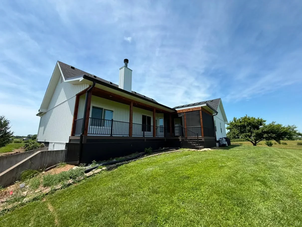 White and black painted farmhouse exterior with covered porch, dark wood beams, and metal railings